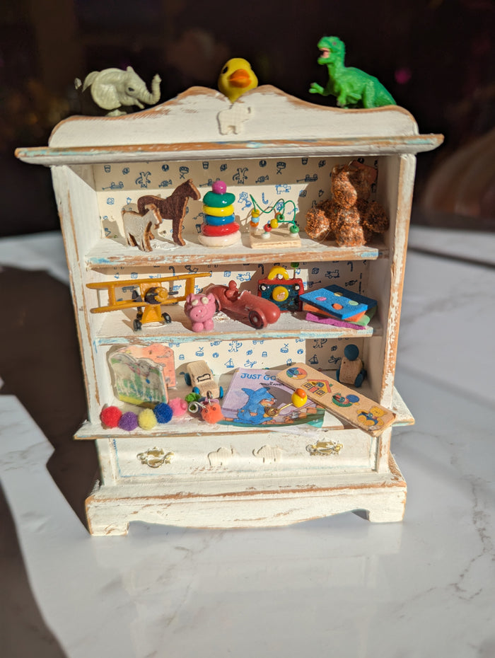 Detailed miniature nursery hutch scene with tiny furniture and accessories, crafted by Detail In Miniature for dollhouse displays.