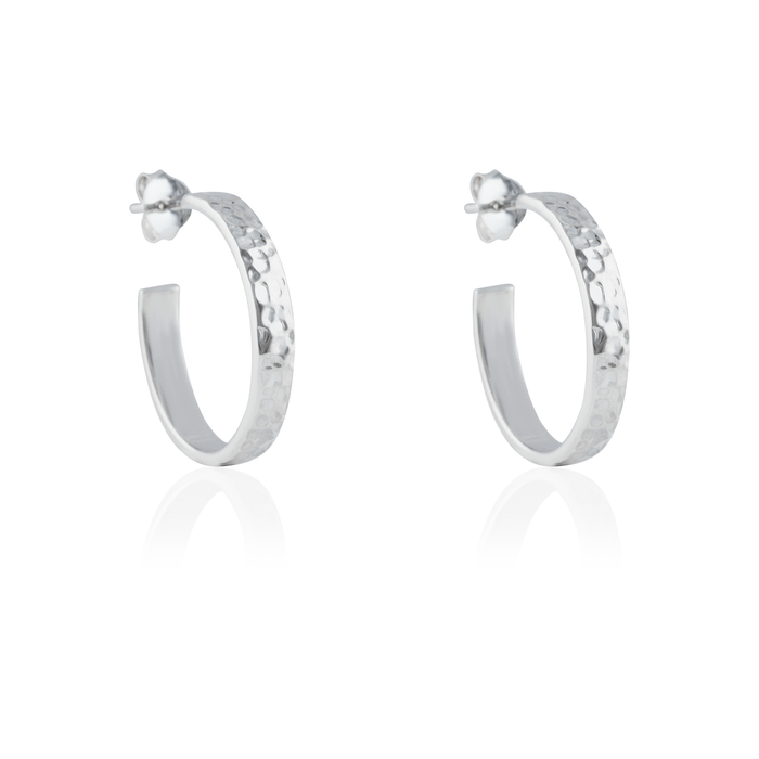 Close-up of a pair of hammered silver hoop earrings with post backings on a reflective white background.