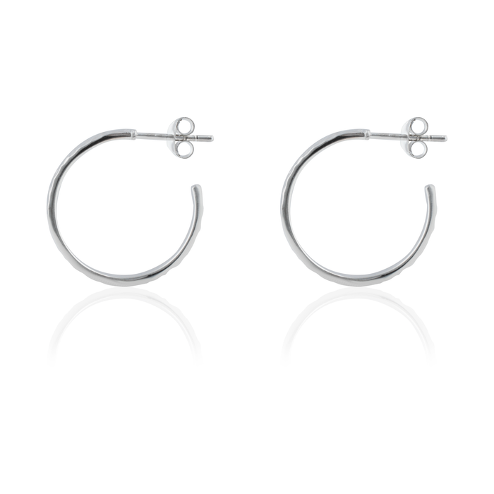 Side view of a pair of hammered silver hoop earrings with post backings on a reflective white background.