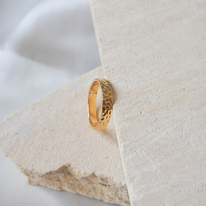 A thin gold hammered ring placed on a beige stone.
