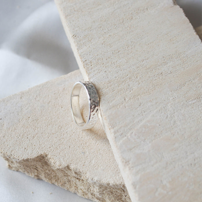 A single narrow, hammered silver ring on a beige stone.
