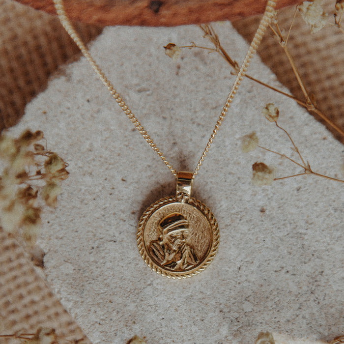 Gold necklace with a pendant on a textured surface with dried flowers