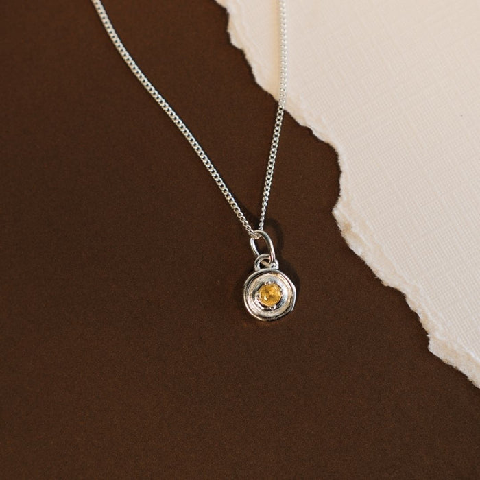 Silver necklace with a yellow gemstone pendant on a brown surface