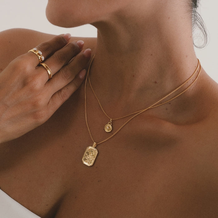 Close-up of a person wearing gold necklaces and rings on a neutral background