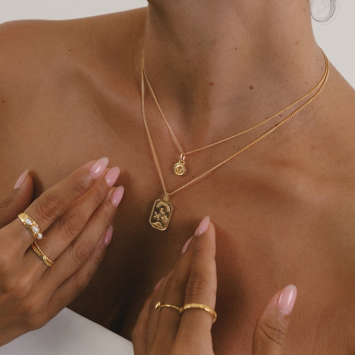 Gold necklace with a pendant on a person's neck, with hands adjusting the jewelry.
