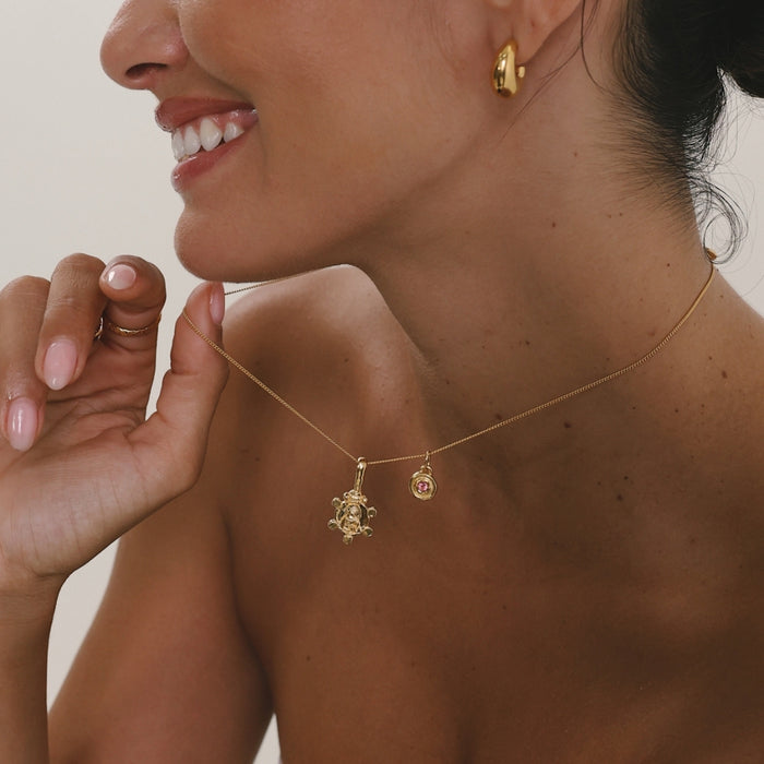 Woman wearing a gold necklace with two pendants, smiling.