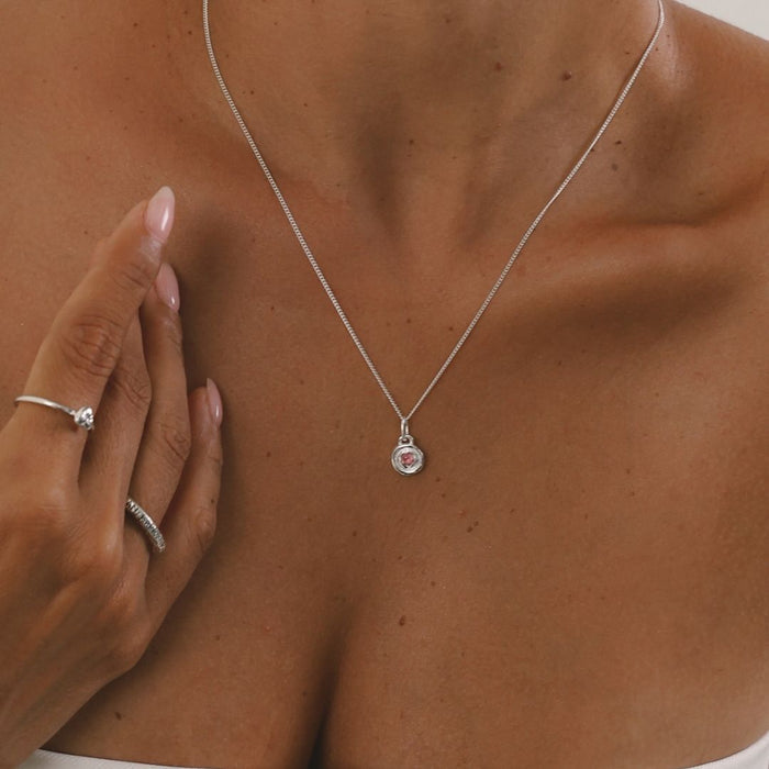 Silver necklace with a heart pendant on a person's neck, hand touching the skin.