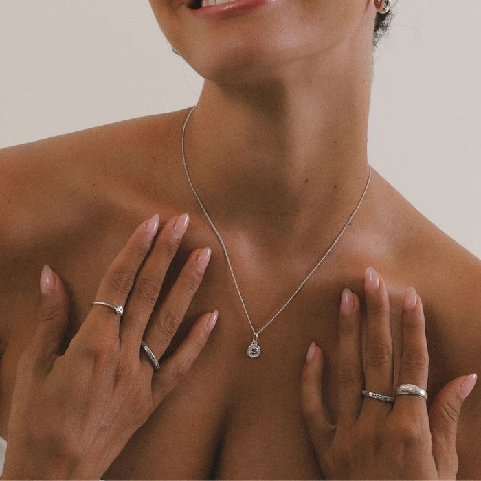Woman wearing a silver necklace with a pendant, hands adorned with rings, on a neutral background