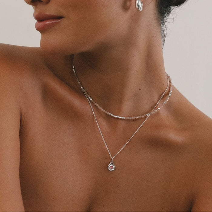Close-up of a woman wearing two necklaces with a neutral background