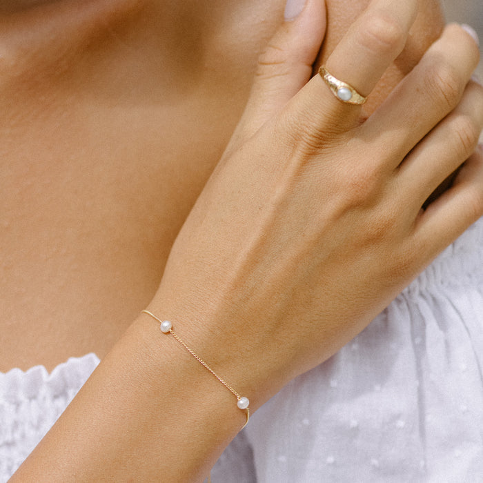 a woman with white dress wearing ring gold on her finger and pearl bracelet gold on her wrist