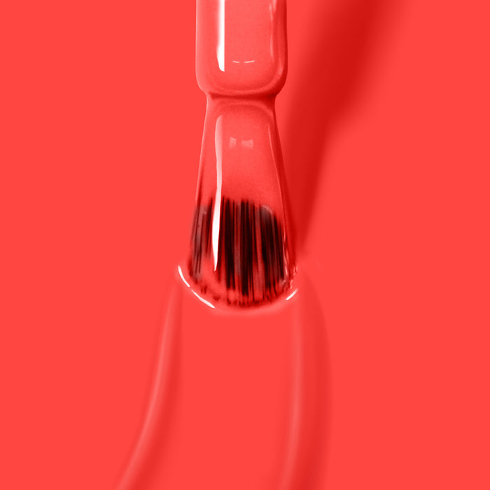 A close-up of a nail polish brush applying LONDONTOWN's Piccadilly Square, an ultra-bright blood orange crème nail polish, against a red background.