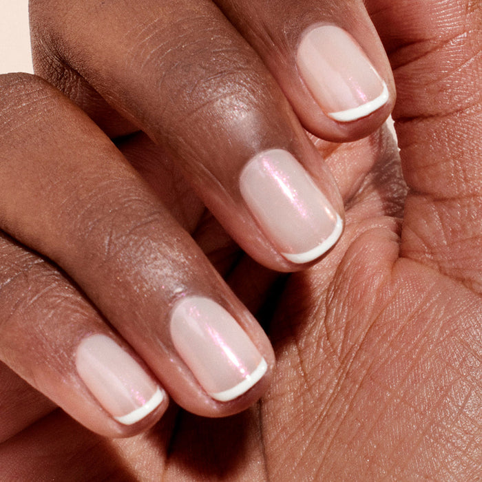 A close-up of neatly manicured nails in a classic French style, elevated by Manucurist's Pink Glazed Effect Powder for a pale pink hue, thin white tips, and a subtle pearlescent sheen.