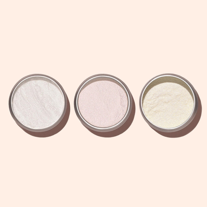 Three small round containers of Manucurist Pink Glazed Effect Powder, in white, light pink, and light yellow shades, are arranged on a pale background, each providing a delicate pearlescent sheen for a subtle glazed finish.