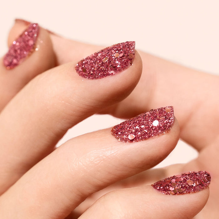 A close-up of almond-shaped nails painted with Manucurist Pink Quartz Biodegradable Glitter. The sparkly, glossy pink hues shimmer against a soft pale background.