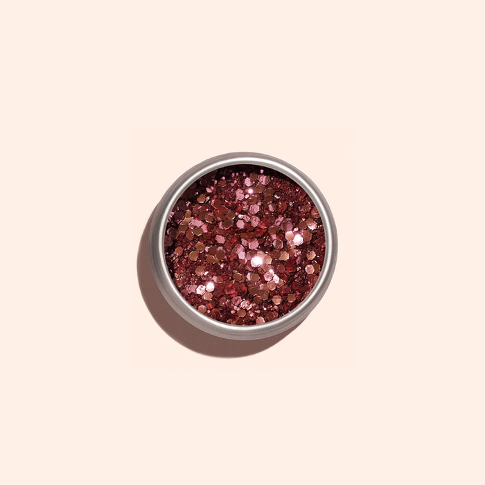 A small round container of Manucurist Pink Quartz Biodegradable Glitter, filled with shiny, chunky rose gold pieces, sits on a light beige background—perfect for adding eco-friendly sparkle to your nail art.