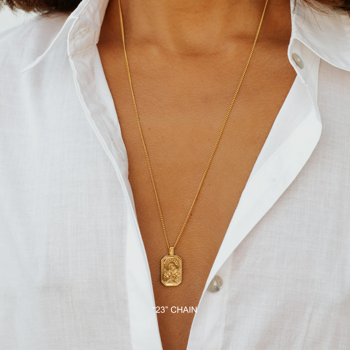 Gold necklace with a pendant on a person wearing a white shirt.