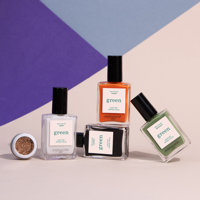Four bottles of Manucurist’s Pumpkin Patch nail polish in clear, orange, black, and green are displayed with a small open container of gold glitter on a purple and beige geometric background—ideal for Halloween nail art.