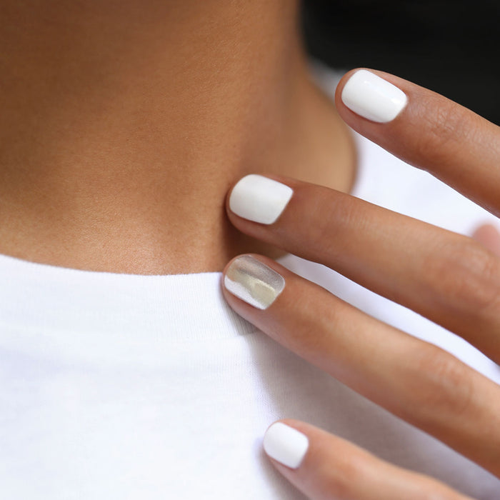A close-up of neatly manicured nails painted with the Manucurist Red, White  Blue Trio, gently touching a collarbone, complements striking red, white, and blue eyeshadow for a bold look.