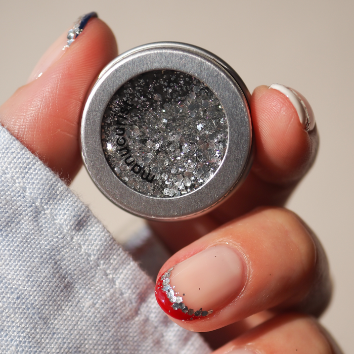 A hand with red and silver glitter nail art holds the Manucurist Red, White  Blue Trio, with red, white, and blue eyeshadow for a vibrant look.