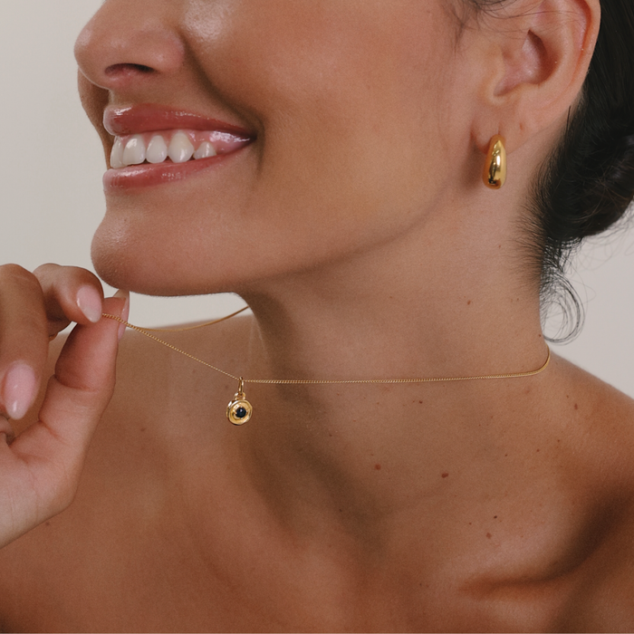 Close-up of a woman wearing gold earrings and a necklace with a pendant.