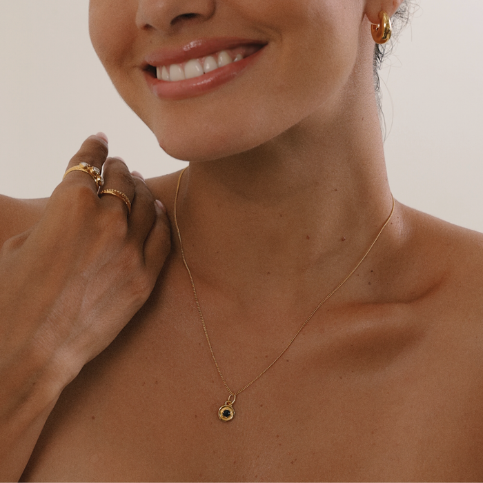 Close-up of a woman wearing a gold necklace with a pendant, with a neutral background.