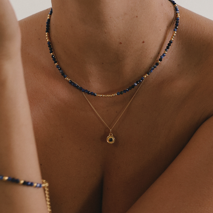 Close-up of a person wearing two necklaces with blue and gold beads.