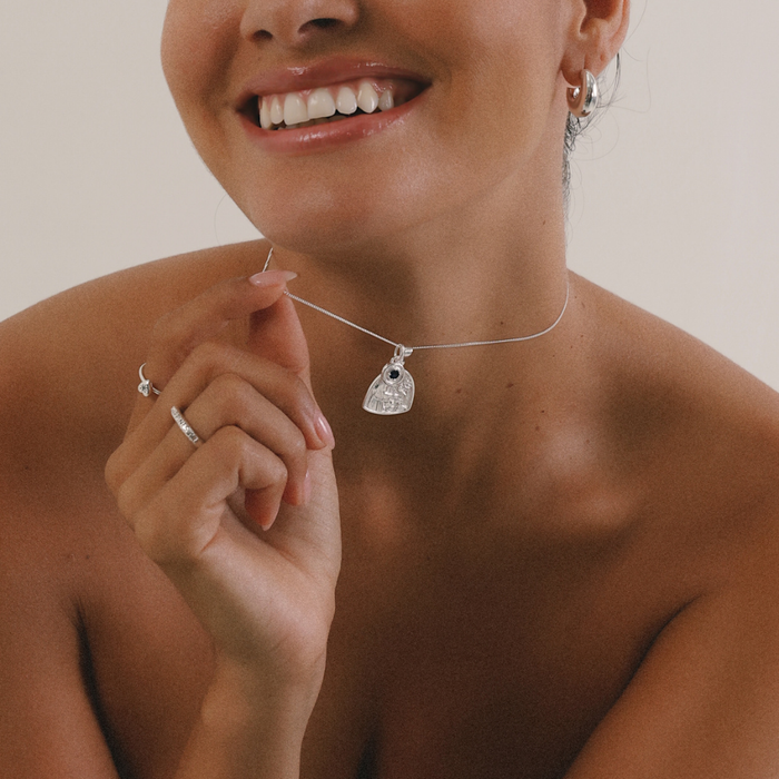 Woman wearing a silver necklace with a pendant, smiling.
