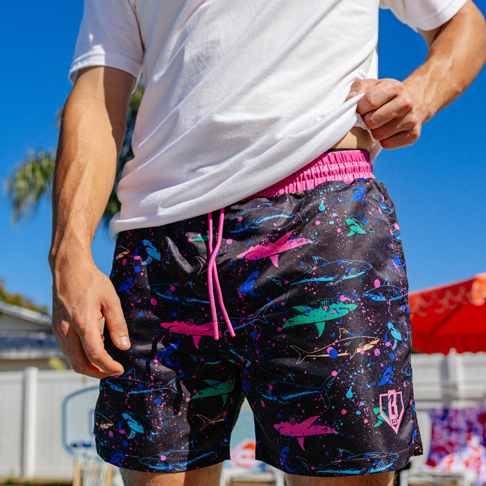 Close-up front view of BL101 neon shark swim shorts on a male model, highlighting the pink waistband and all-over shark print.