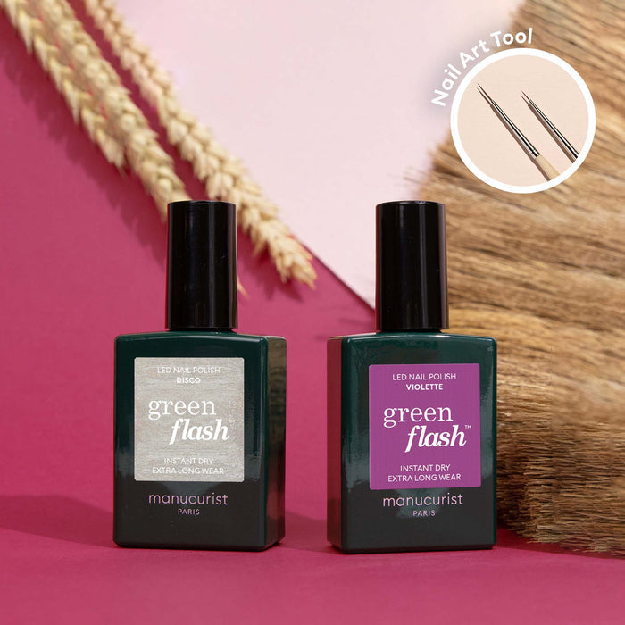 Two bottles of Manucurist’s Shiny Summer nail polish rest on a pink and brown backdrop. A circular inset highlights a Nail Art Brush with fine metal tips, while dried grasses suggest creative Arty Shiny Summer nail art inspiration.