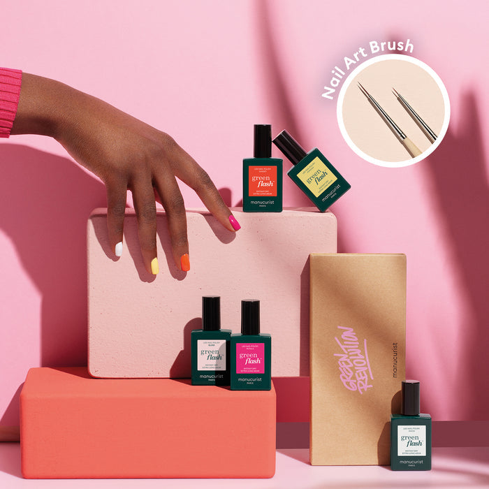 A hand with multicolored nails from Manucurist’s Smile! rests on pink and peach blocks, surrounded by four Smile! bottles and a Nail Art Brush in an inset circle—a bright, stylish setup perfect for summer nail art inspiration.