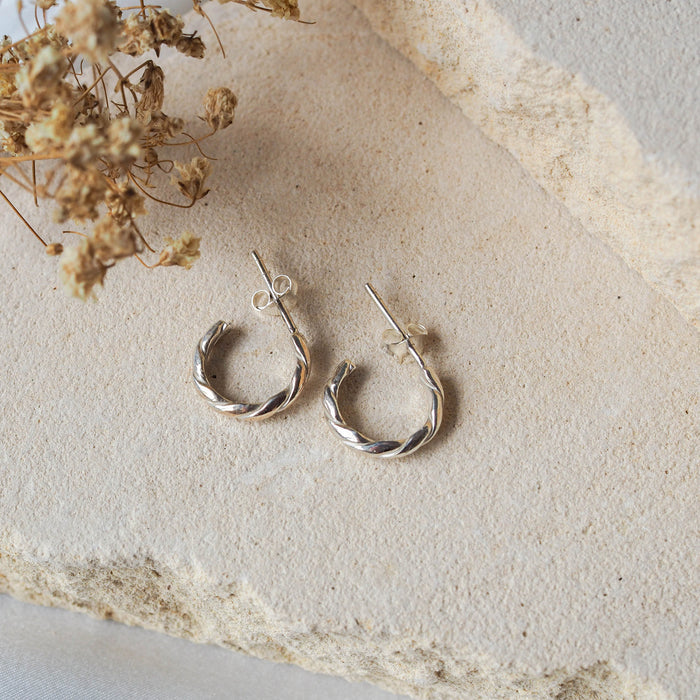 The Hudson Twisted Hoops 12mm - Silver displayed on beige stone with dried flowers
