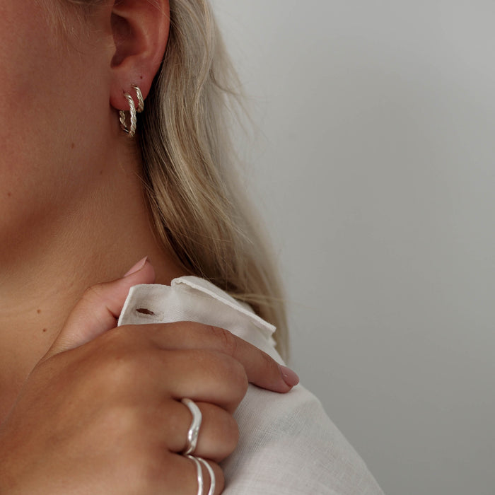 a woman with white shirt wearing  rings silver and hoops earrings  silver