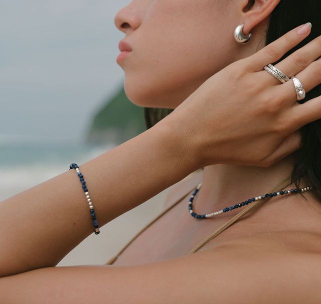 Close-up of hands and neckline highlighting silver rings, bracelet, earrings, and gemstone necklace