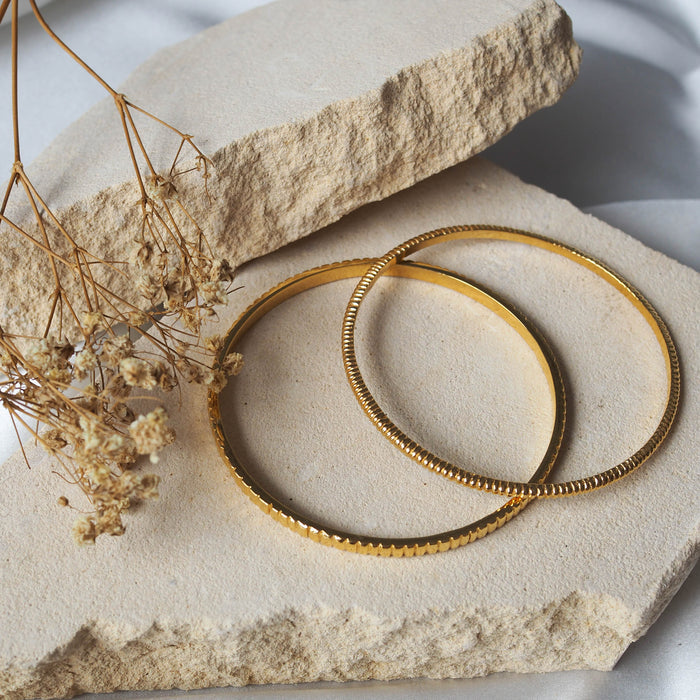 two bracelets gold displayed on beige stone with dried flowers