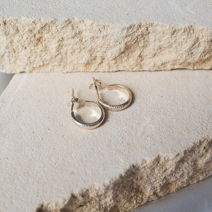 The MET Stripe Thin Earrings 12mm - Silver displayed on beige stone