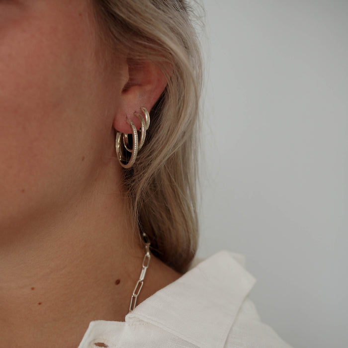 a woman with white shirt wearing  multiple hoops earrings silver