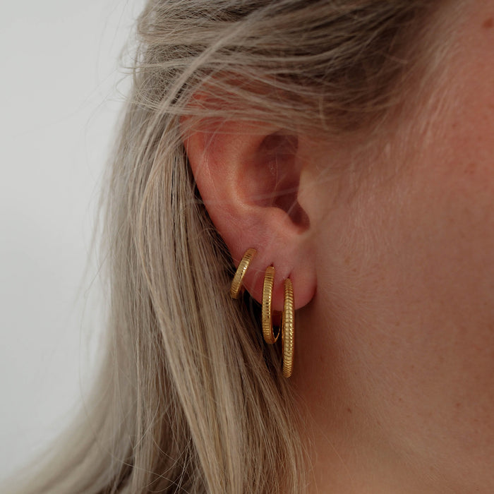 a woman with blonde hair wearing three pieces of hoops earrings gold