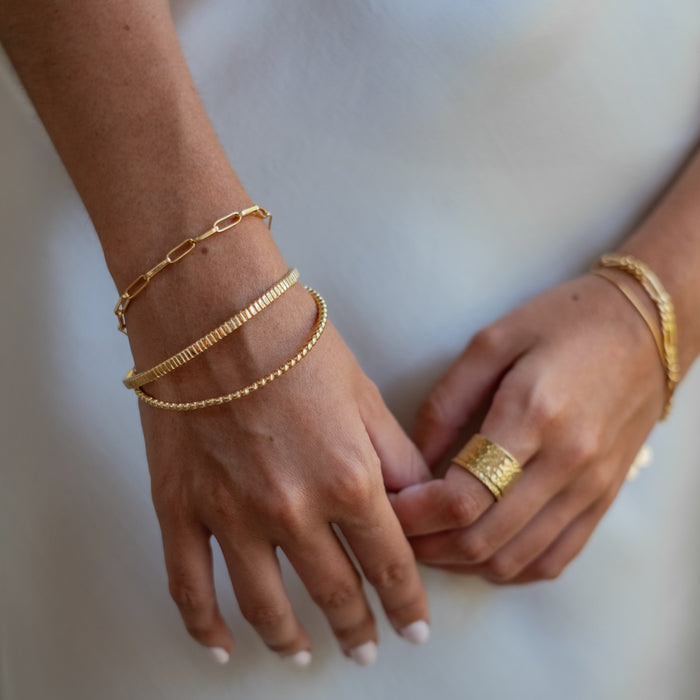 a woman with white dress wearing multiple bracelets gold and rings gold