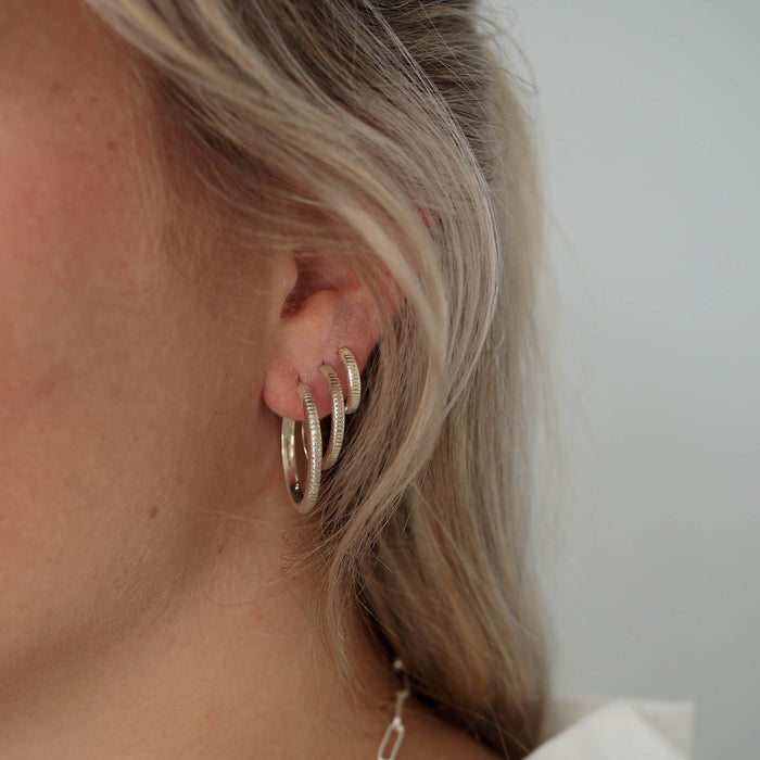 a woman with blonde hair wearing 3 pieces hoops earrings silver