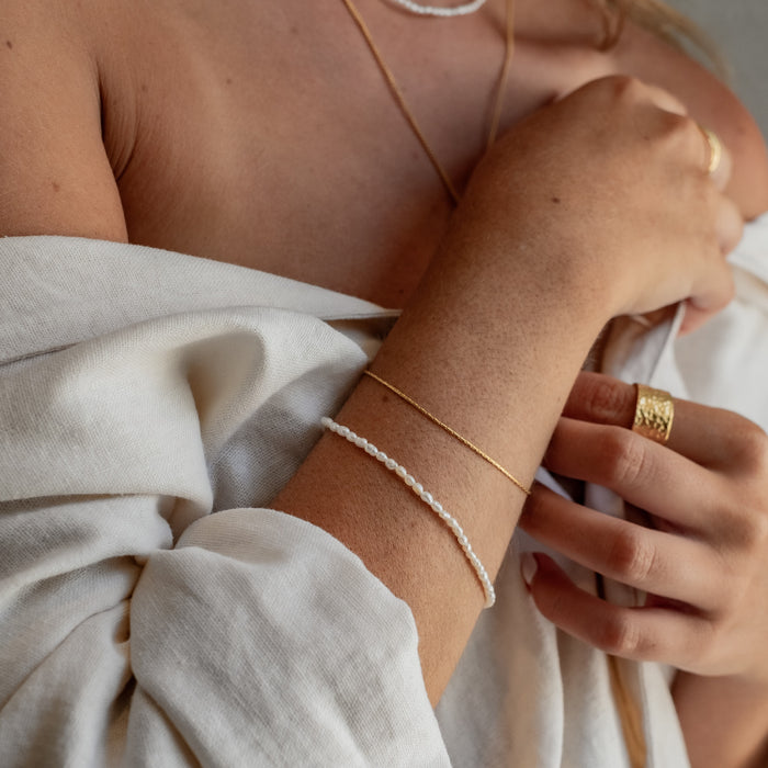 a woman with white shirt  wearing  two bracelets gold ring gold and necklace gold on her