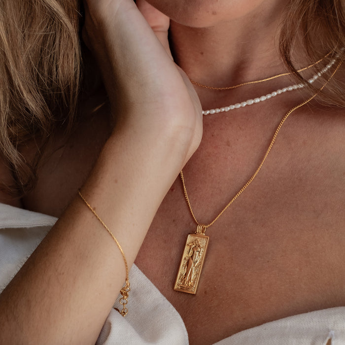 a woman with white  shirt wearing multiple necklaces gold and bracelet gold