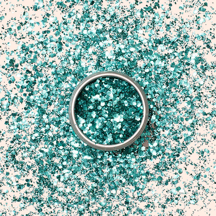 A silver ring sits on a surface sprinkled with Manucurist Turquoise Biodegradable Glitter, creating a sparkling, festive backdrop perfect for nail art inspiration.