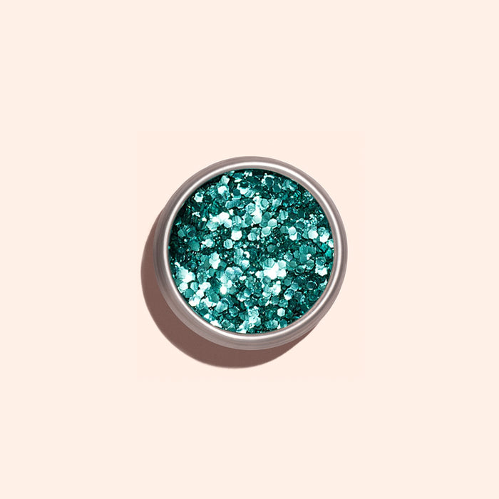 A small round container of Manucurist Turquoise Biodegradable Glitter rests on a plain light beige background, ready to enhance your nail art or gel polish designs.