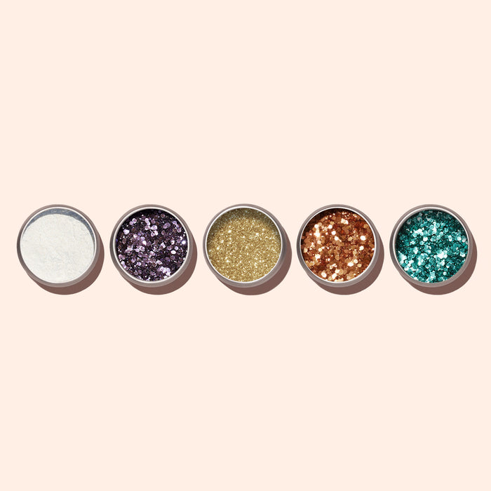 Five small round containers of Manucurist Turquoise Biodegradable Glitter in white, purple, gold, copper, and teal shades—ideal for gel polish or creative nail art—are arranged in a row on a light beige background.