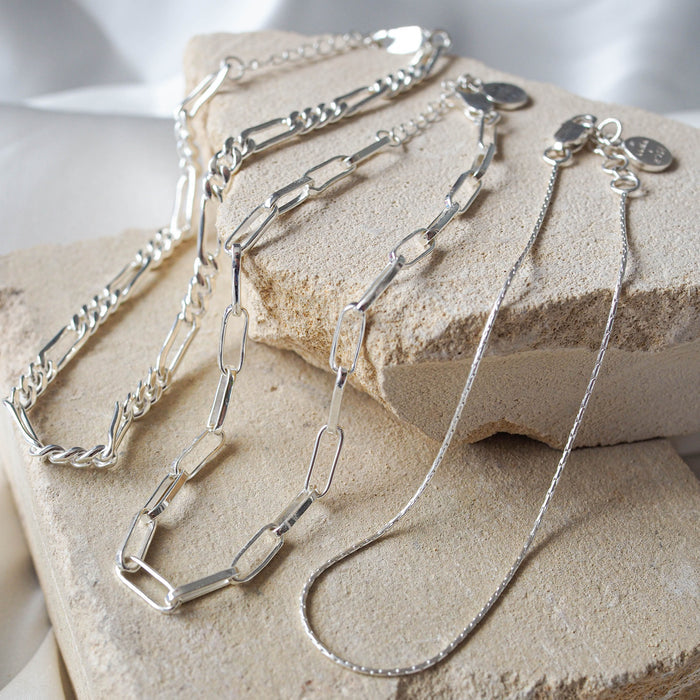 Three silver anklets displayed on beige stone