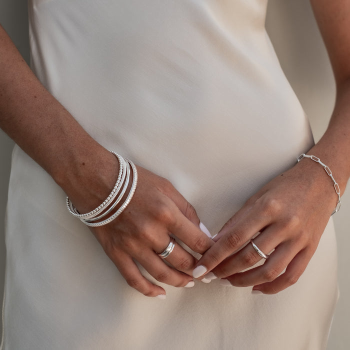 a woman with white dress wearing multiple bracelets silver and ring silver