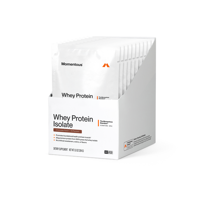 Momentous Whey Protein Isolate box of 10 packets, Chocolate Flavor, on a black background with white packets standing in the open box. Label reads Whey Protein Isolate, The Momentous Standard Signature Spec, and bullets: promotes foundational health and lean muscle; 20g premium protein from 100% grass-fed whey isolate; no artificial sweeteners, colors, or flavors. Dietary Supplement, net wt 9.3 oz (264 g). NSF Certified for Sport.