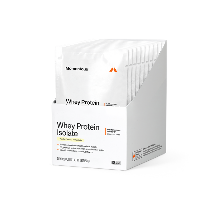 Momentous Whey Protein Isolate box of 10 packets, Vanilla Flavor, on a black background with white packets standing in the open box. Label reads Whey Protein Isolate, The Momentous Standard Signature Spec, and bullets: promotes foundational health and lean muscle; 20g premium protein from 100% grass-fed whey isolate; no artificial sweeteners, colors, or flavors. Dietary Supplement, net wt 8.8 oz (250 g). NSF Certified for Sport.